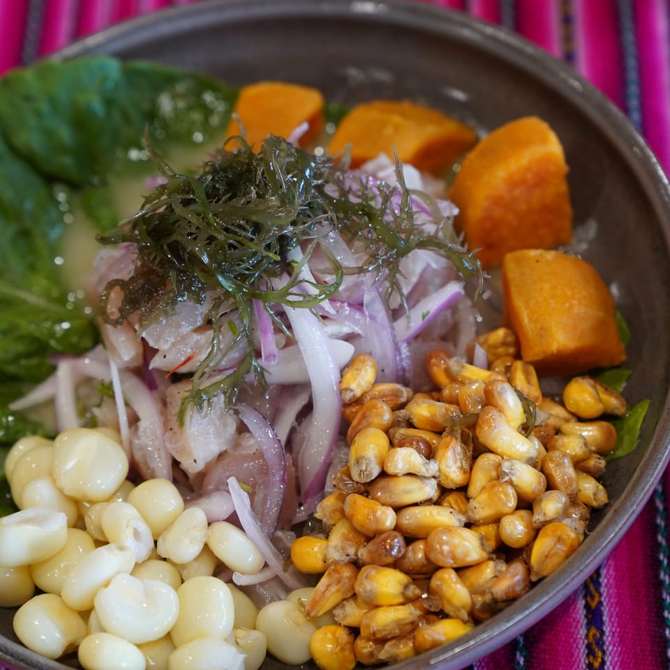 A vibrant ceviche dish with fish, red onion, seaweed, sweet potato, and two types of corn.