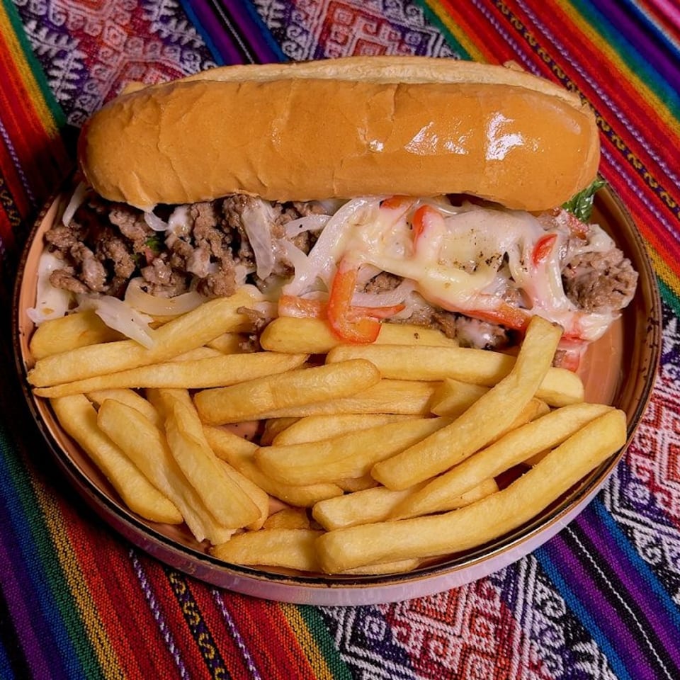 Cheesesteak sandwich with fries on a plate, set against a vibrant, colorful striped fabric.