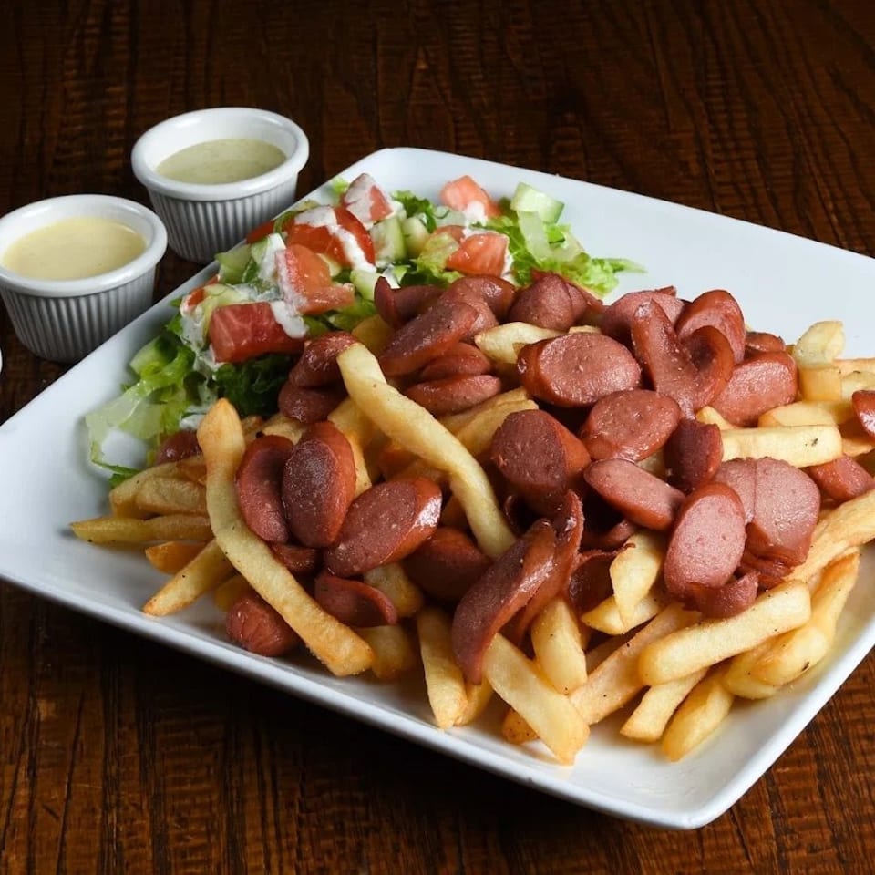A plate of french fries topped with sliced hot dogs, a side salad, and three dipping sauces.