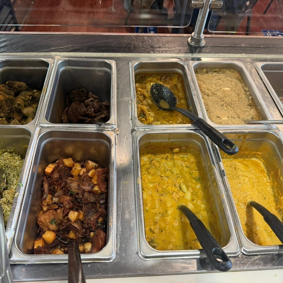A buffet line with various hot dishes in metal trays, including rice, meats, and yellow stews.