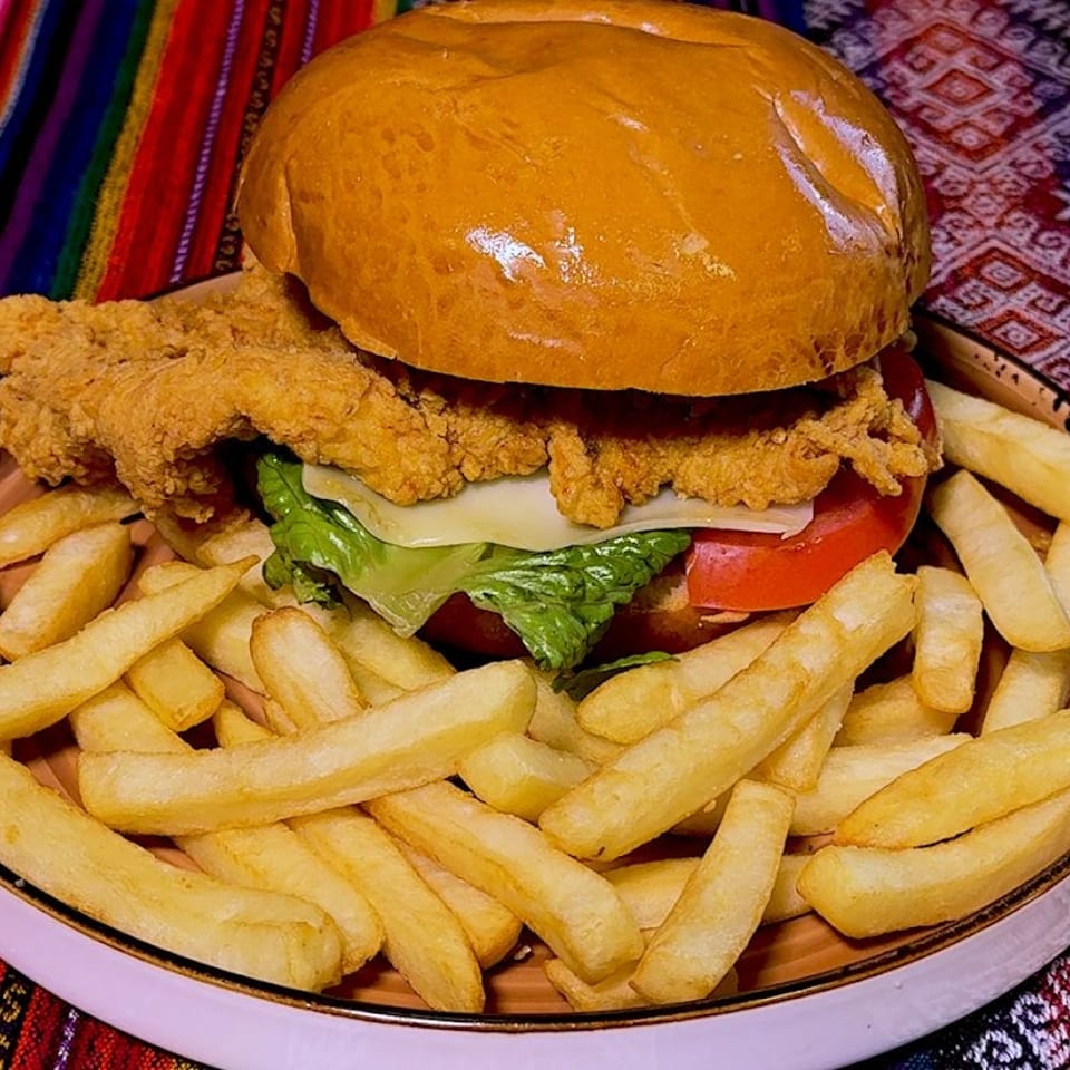 Crispy fried chicken sandwich with lettuce, tomato, and cheese, served with french fries on a colorful patterned tablecloth.